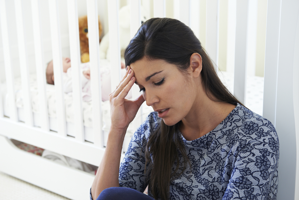 Mum with postnatal depression sitting next to cot