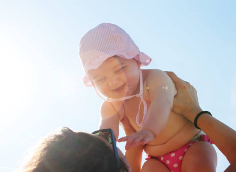 Baby being lifted up by parent into the sunny sky